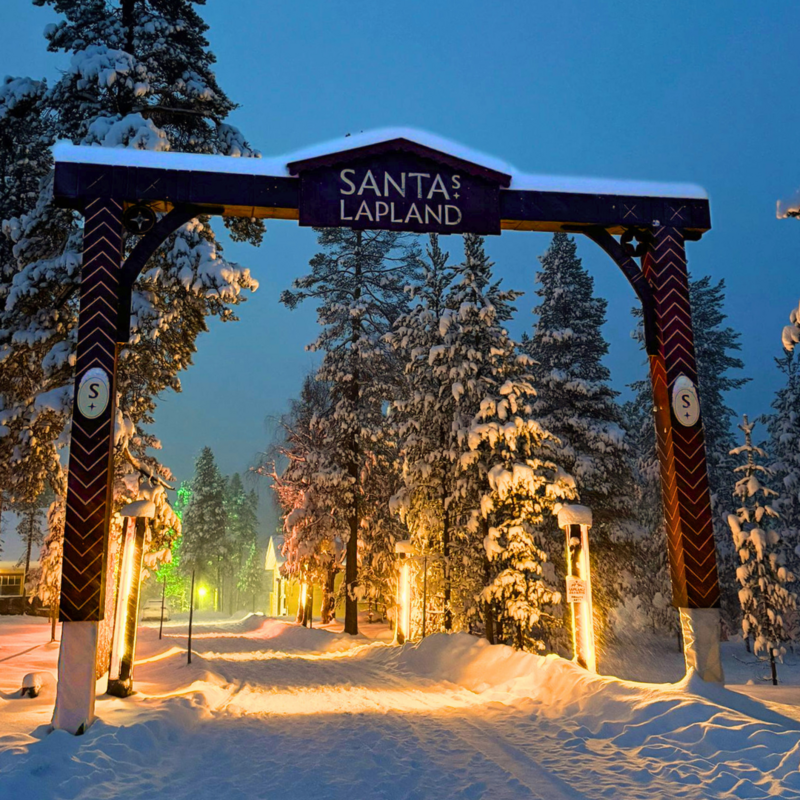 Entrance arch to Santa’s Lapland glowing in the snowy forest on a family Lapland holiday.